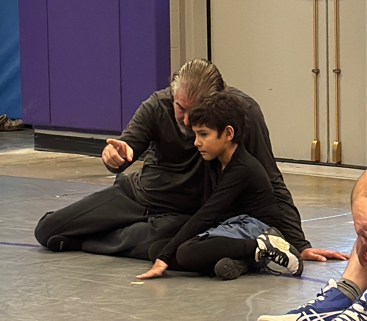 Father coaching his son from the side of the mat during a wrestling session.